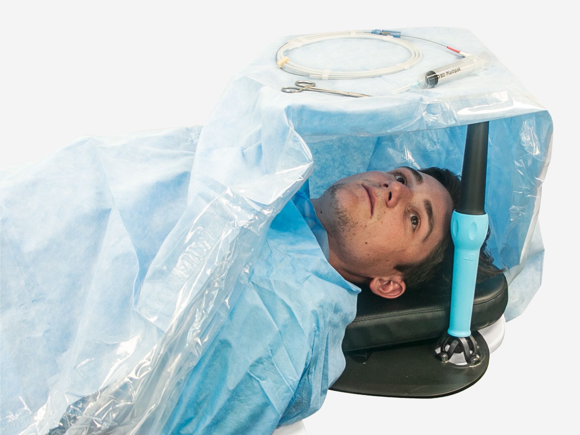 A patient's head visible under a blue surgical drape that forms a tent, with medical tools on it.